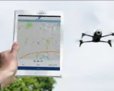 Tablet zeigt eine Karte und Drohnen-Apps. Eine Drohne fliegt im Hintergrund.