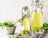 Zwei Flaschen mit selbstgemachtem Waldmeistersirup, dekoriert mit frischen Waldmeisterzweigen und kleinen weißen Blüten.
