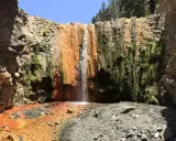 La cascada de colores la Palma, con sus tonos ocres y verdes, cae sobre rocas y vegetación exuberante en un cañón.