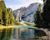 Sentiero da Valdaora al Lago di Braies: acque turchesi, montagne imponenti e pinete rigogliose. Turisti passeggiano sulla riva sabbiosa.