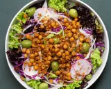 Ensalada colorida con garbanzos fritos crujientes, aceitunas verdes, lechugas variadas, rábano y cebolla morada.