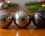 Trois boules de pétanque, deux argentées et une noire, sur une table en bois. Parfait pour un règlement pétanque simplifié.