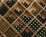 Holzregal mit vielen Flaschen Wein, ideal zum rotwein lagern. Verschiedene Sorten und Farben sind zu sehen.