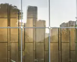 Reflejos dorados de árboles y edificios en un **cristal blindado** moderno, con estructura metálica visible.