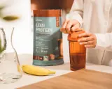 Eine Person bereitet einen Proteinshake zu. Die Packung "Lean Protein" zeigt 17g Protein pro Portion. Die Frage "wie viel protein pulver auf 500 ml" wird durch die Zubereitung beantwortet.