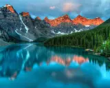 Turkusowe jezioro odbija ośnieżone szczyty gór o zachodzie słońca. W tle gęsty las iglasty. Park narodowy Banff zachwyca.