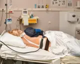 Pacjentka w łóżku szpitalnym z aparaturą medyczną. Widać cewnik z lekiem, co może być związane z pytaniem: epidural co to.