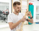 Fizjoterapeuta z wyższej szkoły rehabilitacji w Warszawie pokazuje model kręgosłupa.