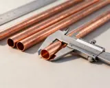Calibrador midiendo las medidas de tubo de cobre. Varios tubos de cobre y una regla metálica en la mesa.