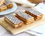 Tre läckra millefeuille-bakelser med lager av smördeg och kräm, toppade med vit glasyr och chokladmönster.