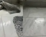 Grå badrumsmattor på marmorgolv. Vattenfläckar syns på golvet, vilket indikerar behov av marmor polering för att återställa glansen.