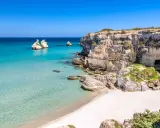 Scogliere calcaree e mare cristallino a Torre dell'Orso centro, con faraglioni che emergono dall'acqua turchese.
