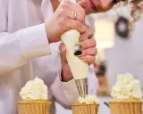 Une pâtissière décore des cupcakes avec une chantilly mascarpone aérienne.