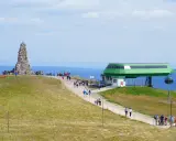 Feldberg: Steinkegel-Denkmal und Seilbahnstation mit Wanderern auf einem grasbewachsenen Hügel.