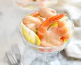 Un delizioso cocktail di gamberi servito in una coppa di cristallo, con una fetta di limone e una salsa rosa cremosa.