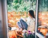 Przytulny jesienny balkon. Dziewczyna w swetrze czyta książkę, otoczona jesiennymi liśćmi i ciepłym światłem lampek.