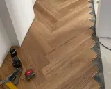 Instalación de suelo de madera en espiga. El rodapié igual que el suelo crea un acabado moderno y continuo. Herramientas de instalación a la vista.