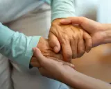 Dwie dłonie, starsza i młodsza, splatają się w geście wsparcia. Zastanawiasz się, komu przysługuje zasiłek za opiekę nad osobą starszą?
