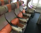 Fotele w samolocie linii lotniczych Emirates, z pomarańczowymi poduszkami i zagłówkami, gotowe na podróż.