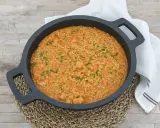 Arroz cremoso con gambones, adornado con cebollino fresco, servido en una paellera sobre una mesa de madera.