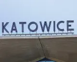 Napis "KATOWICE" z niebieskimi neonami na tle nieba, nad betonową konstrukcją.