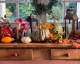 Décoration automne facile à faire : citrouilles, lanternes, fausses champignons et feuilles d'automne sur un buffet en bois devant une fenêtre.