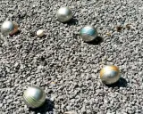 Boules de pétanque argentées, certaines rayées de couleurs vives, reposent sur un lit de gravier gris. Le jeu de pétanque est prêt à commencer.