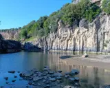 Un'oasi naturale nella Tuscia: un fiume serpeggia tra imponenti pareti rocciose ricoperte di vegetazione, creando uno scenario suggestivo.