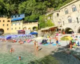 Ein idyllischer **Geheimtipp Italien Strand** mit bunten Sonnenschirmen, sonnenbadenden Menschen und kristallklarem Wasser vor malerischer Kulisse.