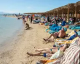 Słoneczna plaża w Egipcie w maju. Ludzie odpoczywają na leżakach pod palmowymi parasolami, ciesząc się piękną pogodą.