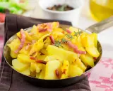 Patatas al microondas con trocitos de bacon crujiente y romero fresco, servidas en una sartén metálica. ¡Un plato rápido y delicioso!