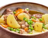 Un reconfortante ragout de ternera con patatas, zanahorias y guisantes en un cuenco rústico.
