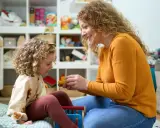 Mama z córką bawią się w pokoju pełnym zabawek. Czy urlop wychowawczy wlicza się do stażu pracy? To pytanie nurtuje wiele mam.