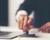 Dłoń z pieczątką, gotowa do złożenia podpisu na akcie poświadczenia dziedziczenia.