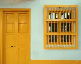 Une porte et une fenêtre avec un encadrement de porte couleur différente, le tout peint en jaune vif sur un mur blanc texturé.