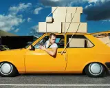 Hombre en coche amarillo cargado de cajas, preguntándose cuanto peso aguanta un coche.