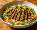 En skål med asiatisk biffsallad med nudlar, strimlad biff, gurka, morötter, mynta och jordnötter.