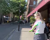 Mujer rubia con una camiseta blanca y pantalones cortos grises, su imagen muestra una **aberración cromática** con bordes verdes y rosados.