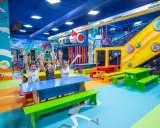 Un grupo de niños alegres levanta las manos en un vibrante centro comercial con juegos para niños, con toboganes, túneles y coloridos muebles.