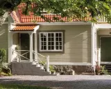 Ett charmigt hus med tegelrött tak och ljusgul fasad, redo att måla om huset. En stor ek skuggar entrén.