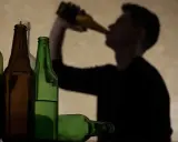Sylwetka mężczyzny pije z butelki. Obok stoją puste i pełne butelki. Ile trzyma 250 ml wódki?