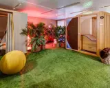Une salle de pause originale avec un gazon synthétique, une cabine en bois, des plantes et un fauteuil de massage.