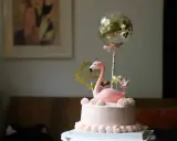 Różowy tort z flamingiem, złotymi serduszkami i koroną. Balon z konfetti dodaje magii. Idealny pomysł, jak udekorować tort na wyjątkową okazję.