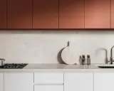 Crédence de cuisine moderne avec placards cuivrés, plan de travail en marbre clair, plaque de cuisson, évier et ustensiles.