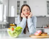 Femme triste face à une salade et des donuts, pensant aux aliments à éviter pour la dermite séborrhéique.