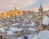 Matera innevato, un incanto tra i **posti da visitare in inverno Italia**. Case antiche e chiese sotto la neve, con il sole che illumina il paesaggio.