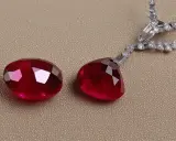 Due magnifiche pietre rosse, tagliate a goccia e ovali, brillano accanto a una collana di diamanti scintillanti.