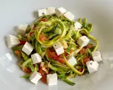 Spaghetti di zucchine freschi con pomodoro e cubetti di feta, conditi con pepe nero.