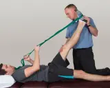 Physiotherapeut hilft Mann bei der Dehnung des Beins mit einem Band. Sanfte Gymnastik bei Bandscheibenvorfall zur Linderung.