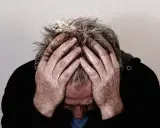 Uomo con le mani tra i capelli grigi, testa china, espressione di profonda preoccupazione. Mala tempora currunt sed peiora parantur.